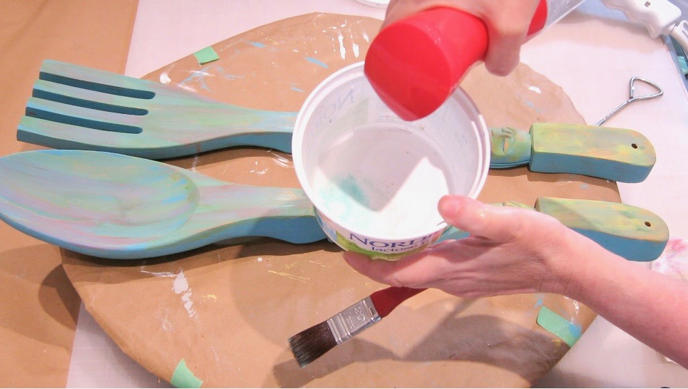 Watering down Terra Clay paint in a plastic container with wooden spoon and fork in background