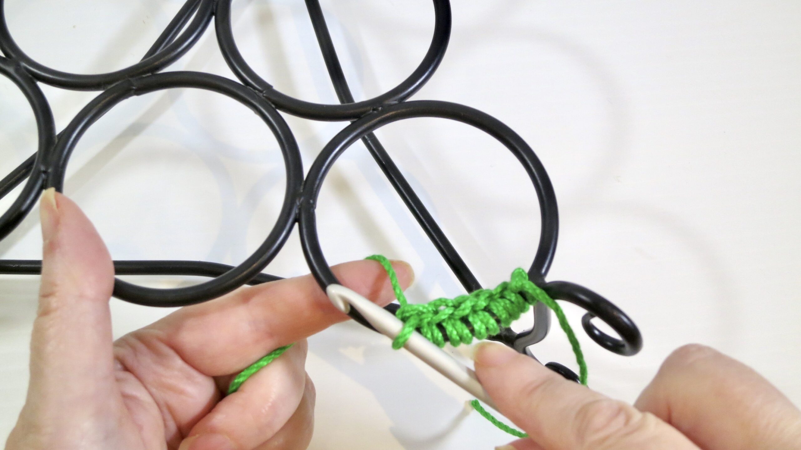 Hand crocheting green yarn onto rings of christmas plant decor