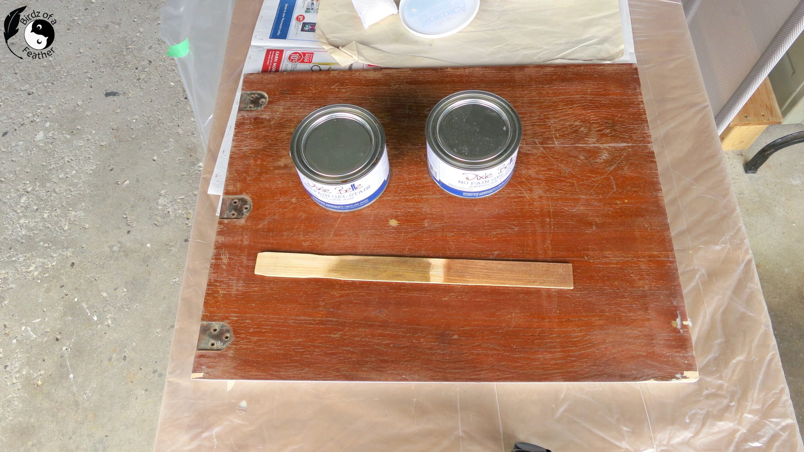 Two tins of stain on top of wood sewing table top with paint stick showing two colours of stain