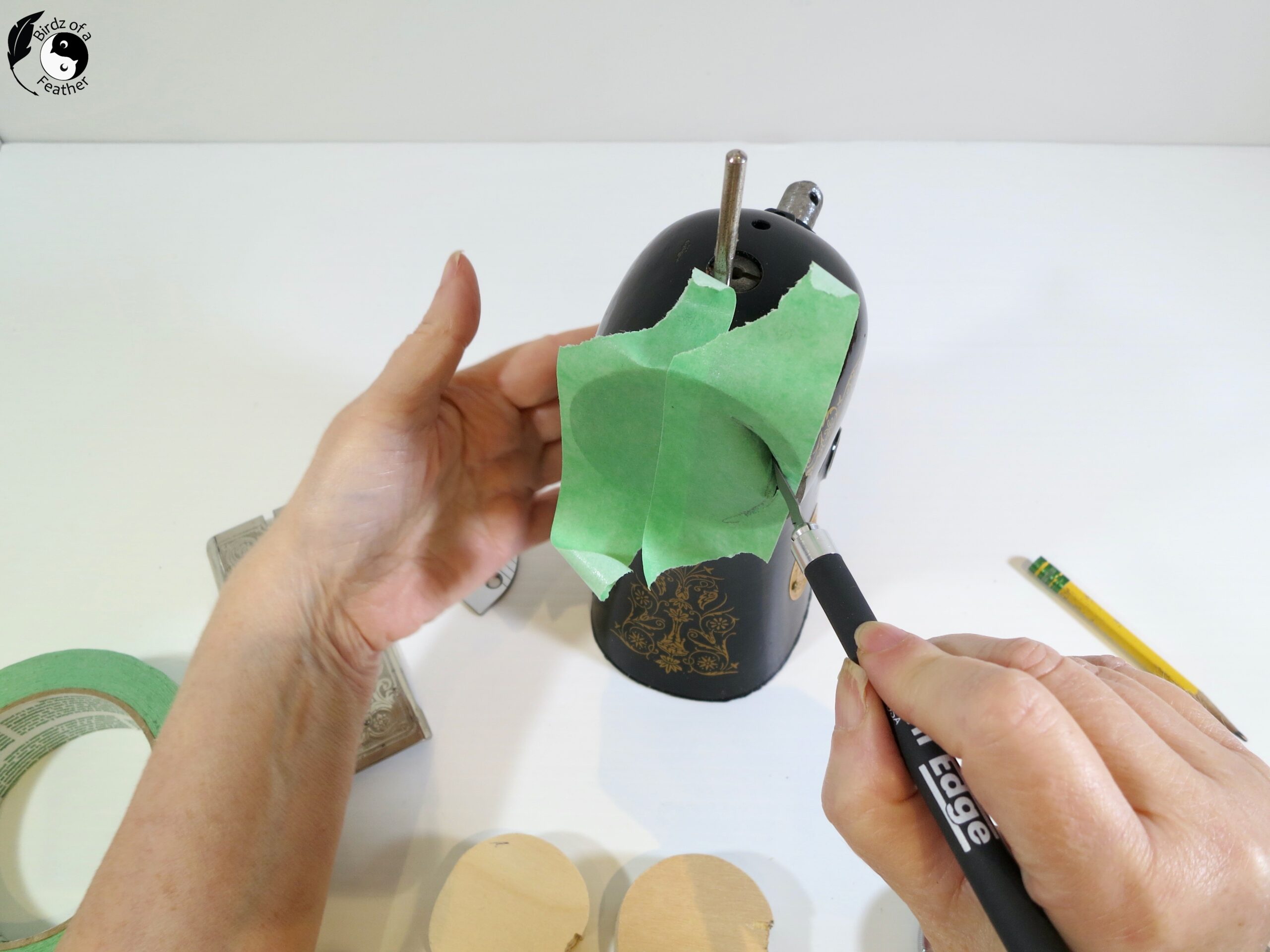Green painters tape over one end of the cut sewing machine with an X-acto knife cutting around the inside 
