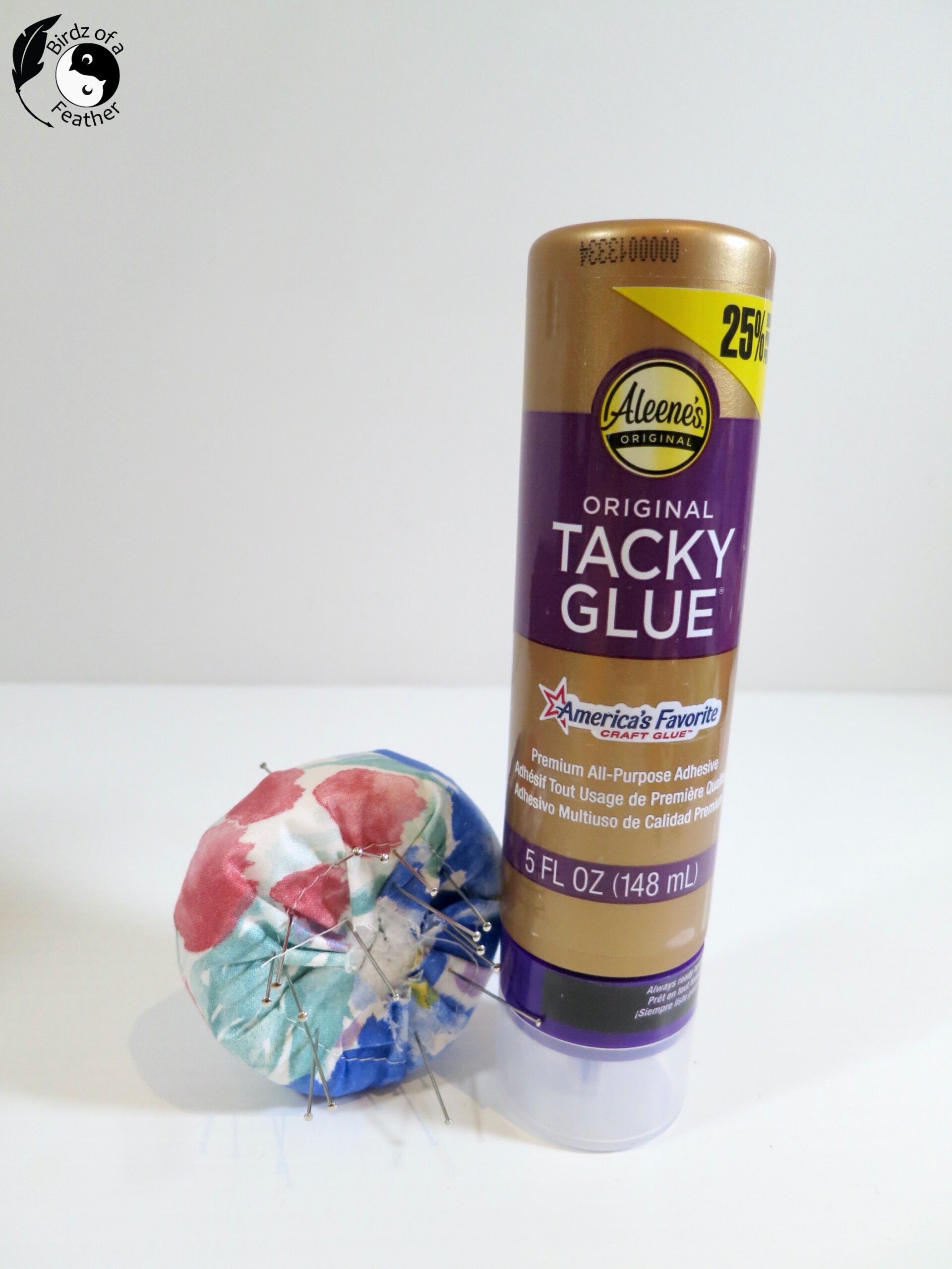 Fabric wrapped foam with pins sticking out and container of glue on table