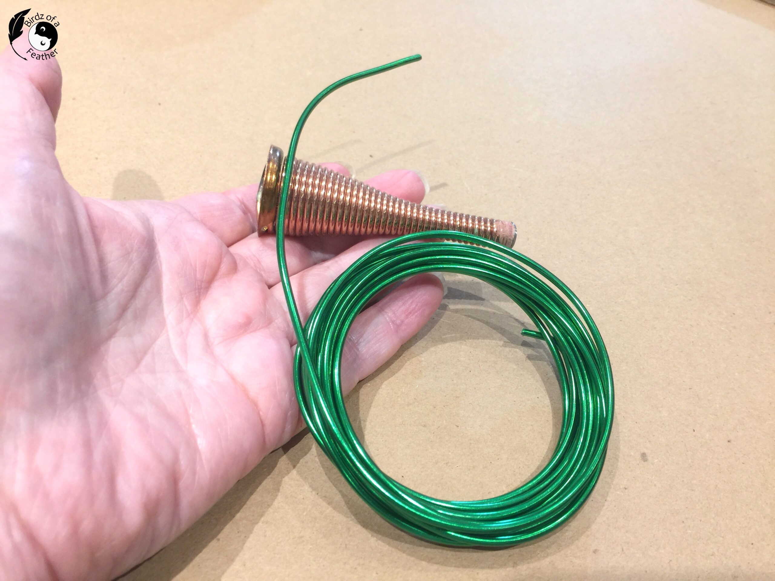 Hand holding a wire door stop and green aluminum wire