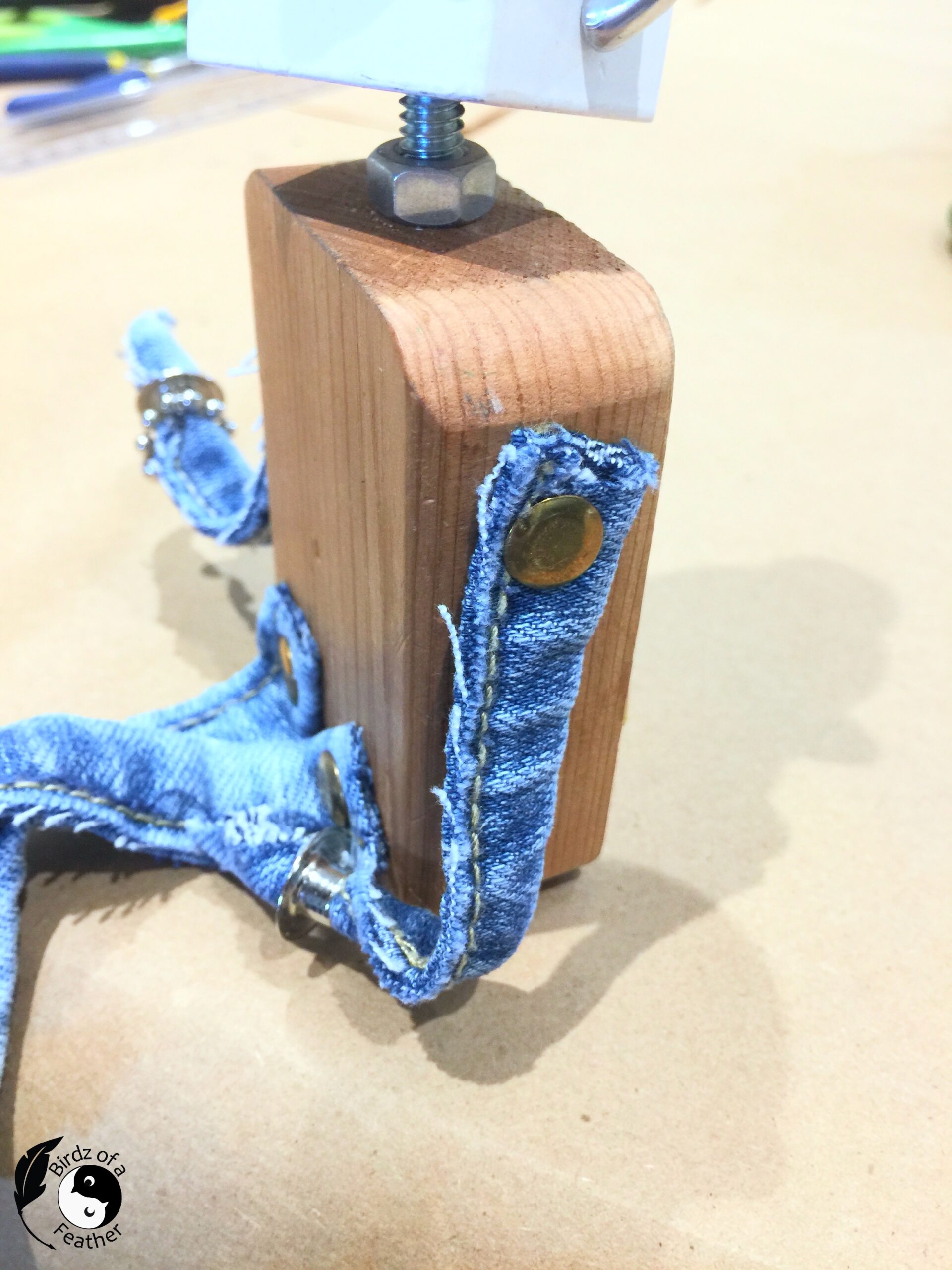 Close up of side of scrap robot showing denim scraps fastened onto wood bod with upholstery tacks