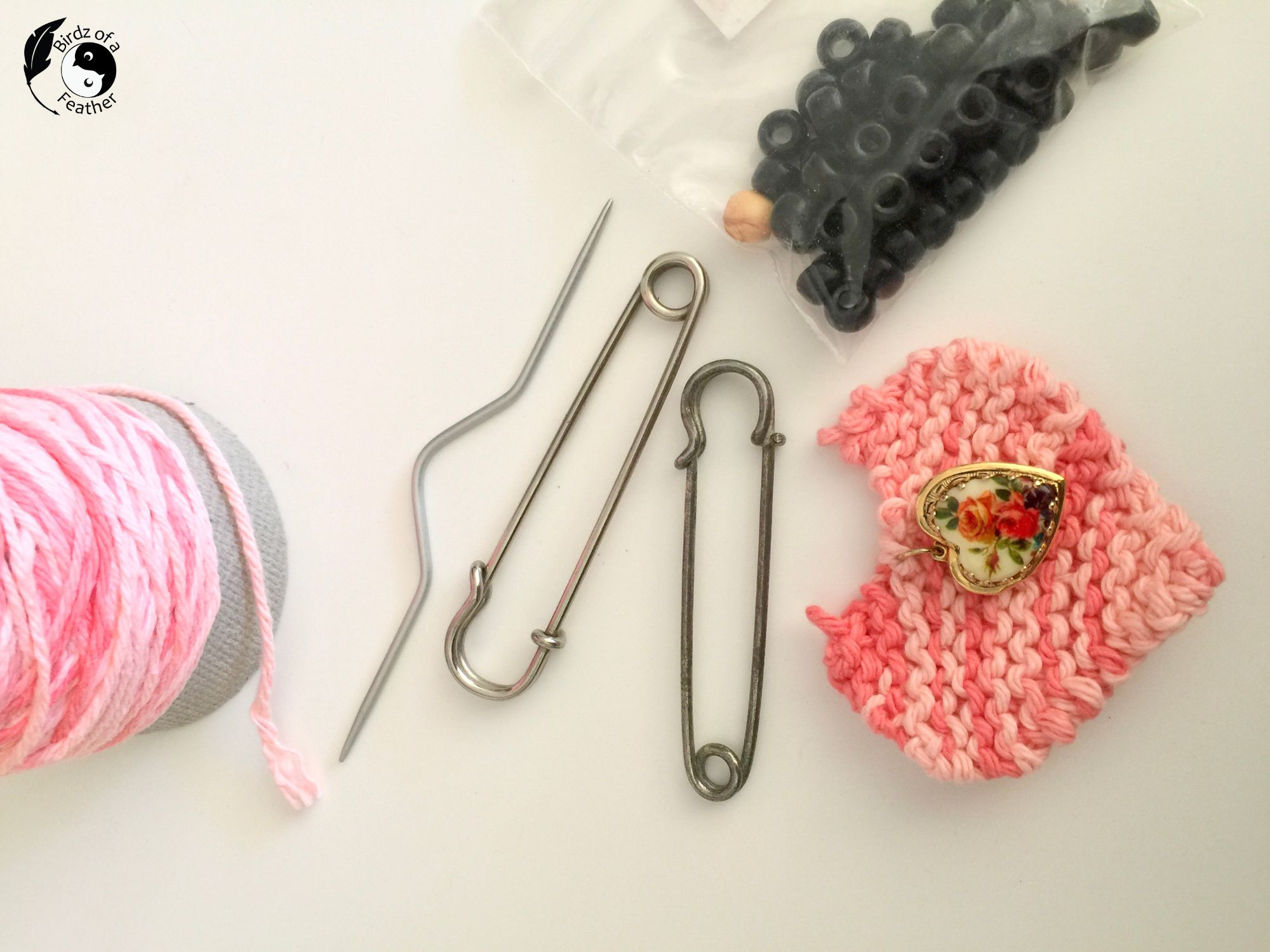 Cable knitting needle, black beads, pin yarn, kilt pins, knit heart and heart locket on table