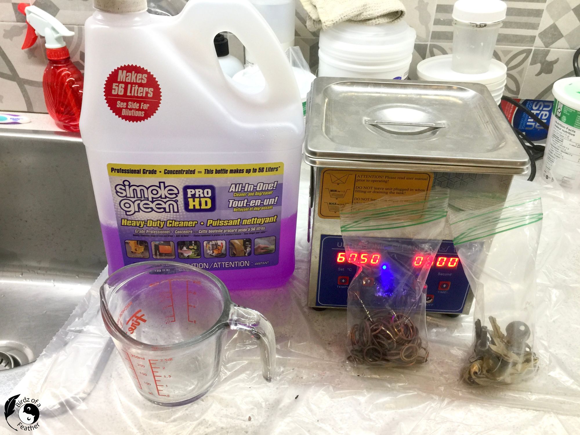 Container of simple green beside an ultrasonic cleaner with buttons and washers separated into bags in the forefront.