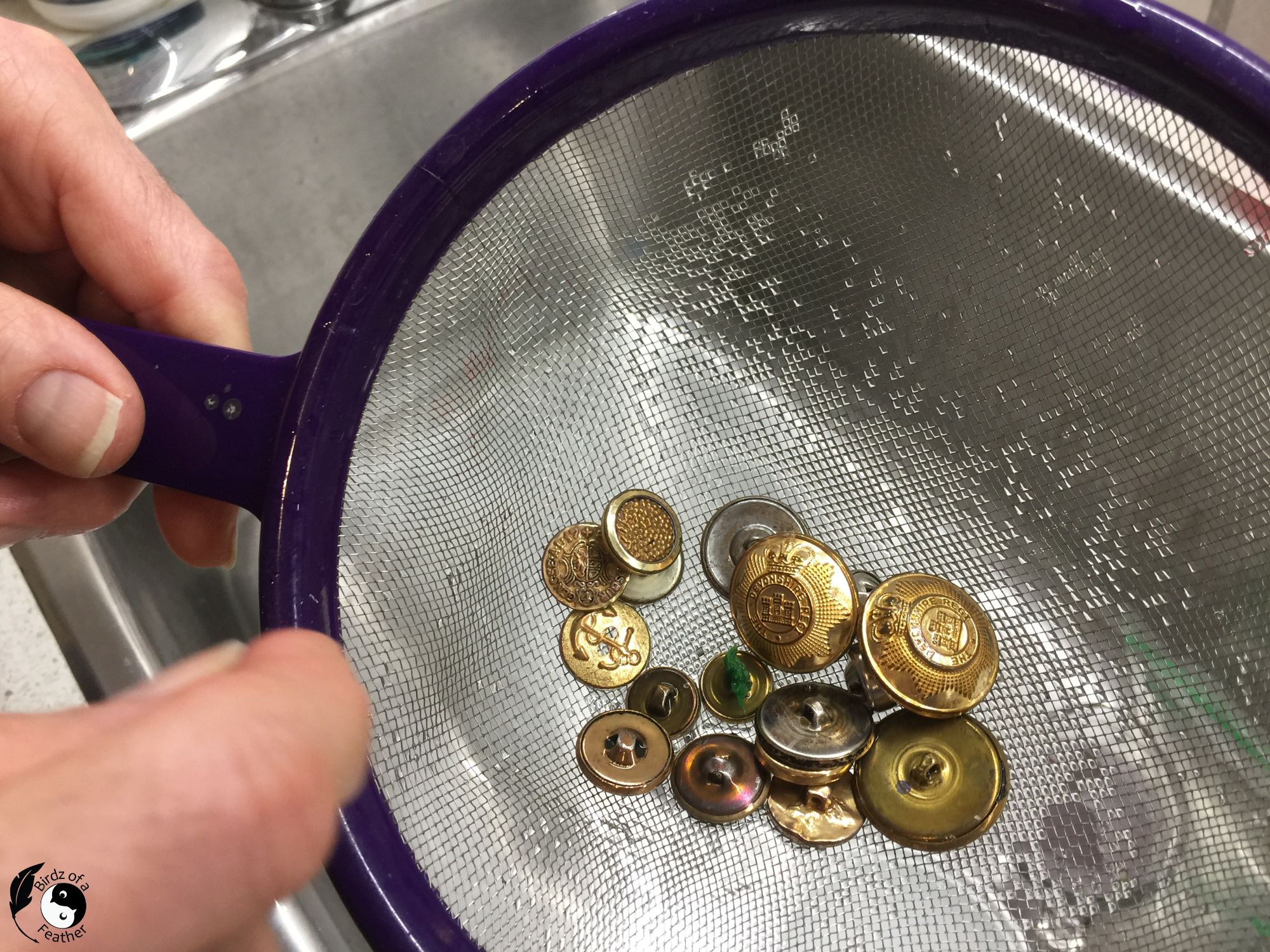 Rinsing the vintage brass buttons in a strainer over the sink